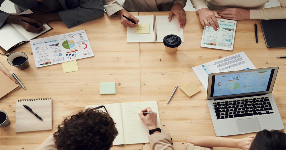 A group of researchers with laptops and documents around a table collaborating on a project.