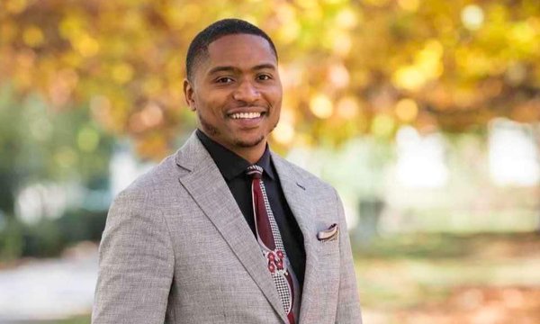 black man wearing suit standing outside with fall leaves on trees