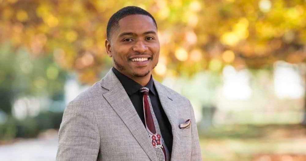 black man wearing suit standing outside with fall leaves on trees