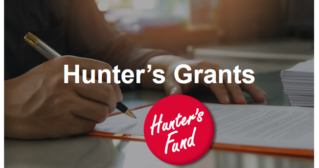 Hunter's Grants Logo in red and white color, placed over a hand writing on a piece of paper