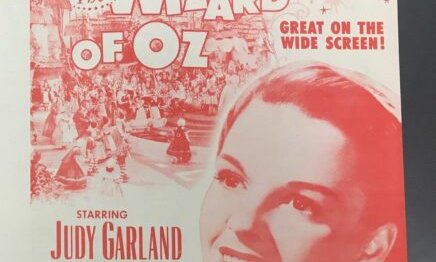 White and red poster advertising The Wizard of Oz film and picturing Judy Garland.