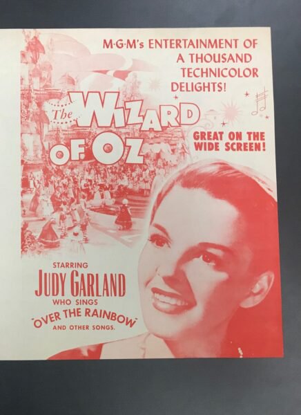 White and red poster advertising The Wizard of Oz film and picturing Judy Garland.