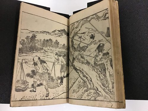 Image of a book opening with a woodblock image that takes up both pages and has a man walking through a landscape with a pole over his shoulders that supports two hanging baskets