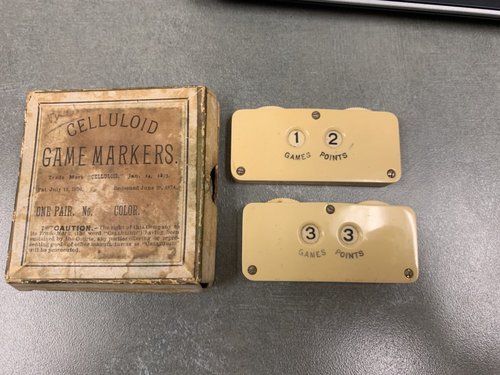 Cardboard brown box with two tan colored celluloid game markers.