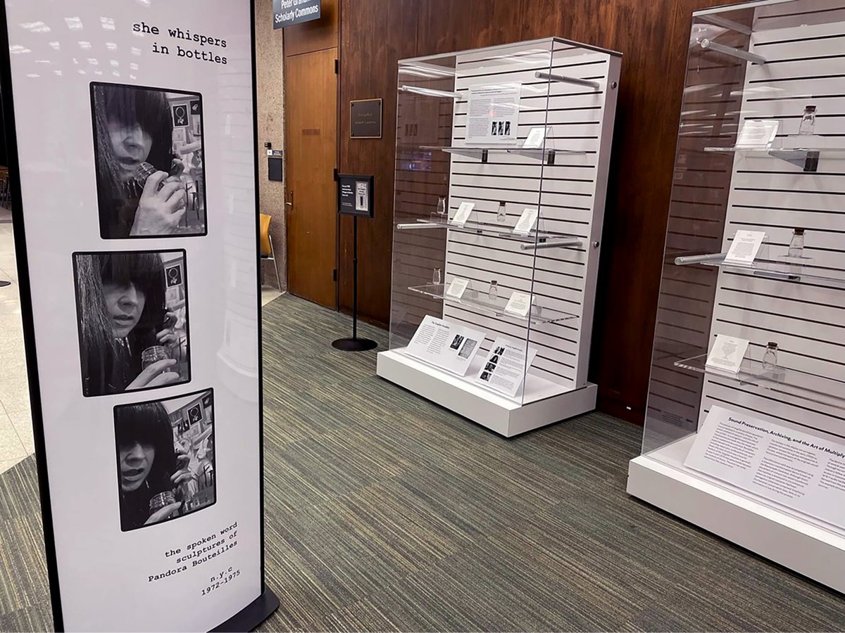 poster with words "she whispers in bottles" and three square photos below, next to two glass display cases