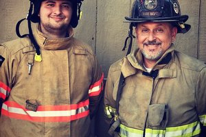 Jared Anderson and his dad Brian Anderson, both in turnout gear smile for a photo
