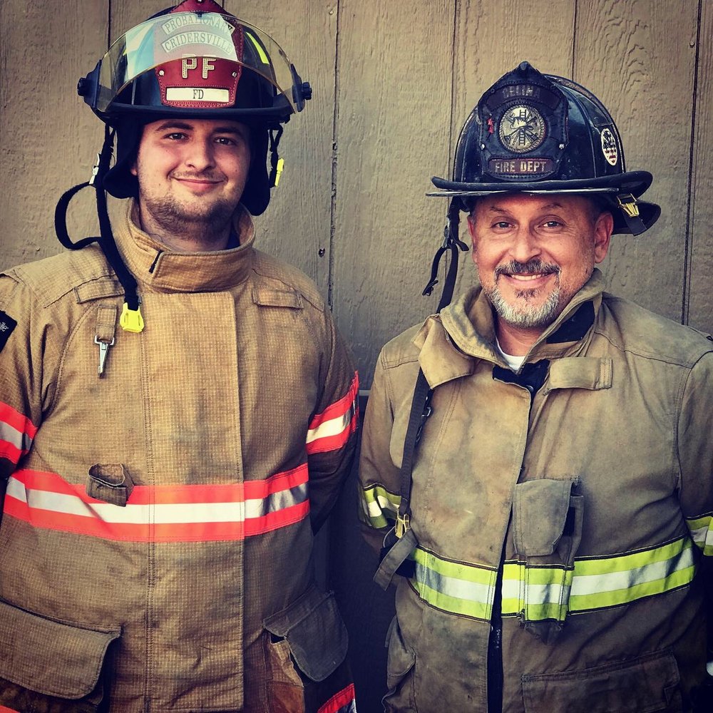 Jared Anderson and his dad Brian Anderson, both in turnout gear smile for a photo