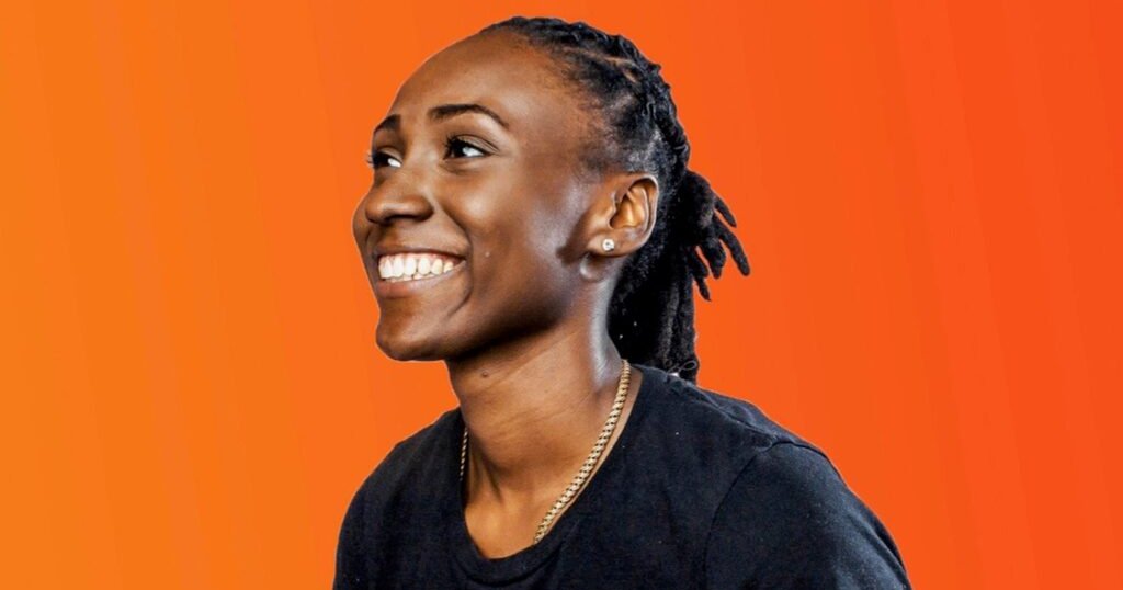 Kelsey Davis smile for a photo against an orange background