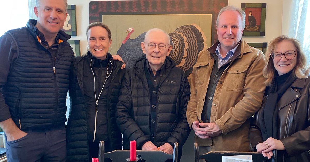 5 people standing behind table posing, with artist painting behind them.