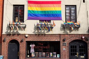 LGBTQ flag and smaller flags hanging above the door and window sign of the Stonewall Inn