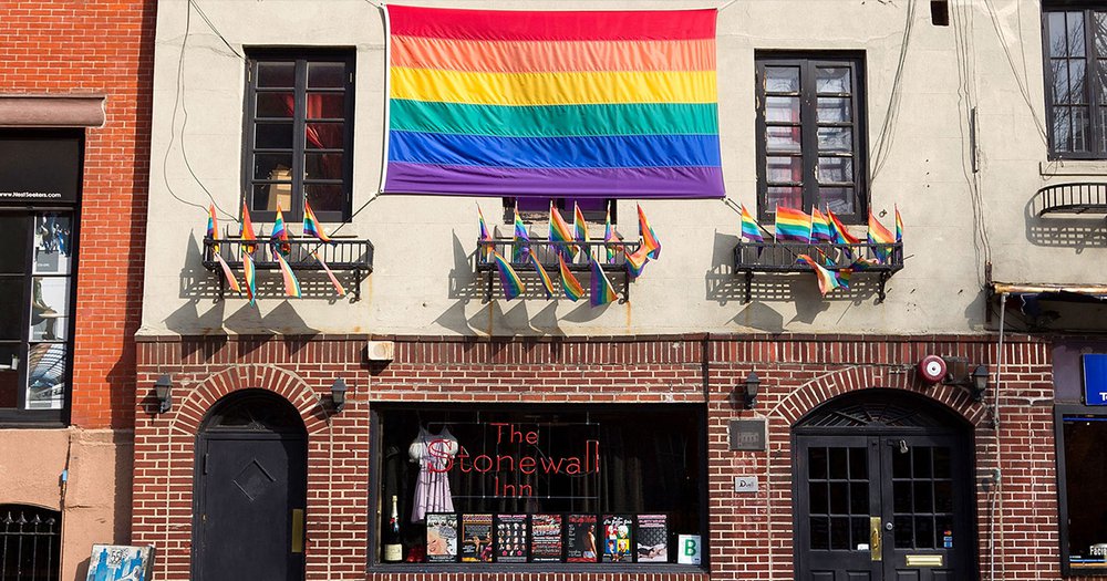 LGBTQ flag and smaller flags hanging above the door and window sign of the Stonewall Inn