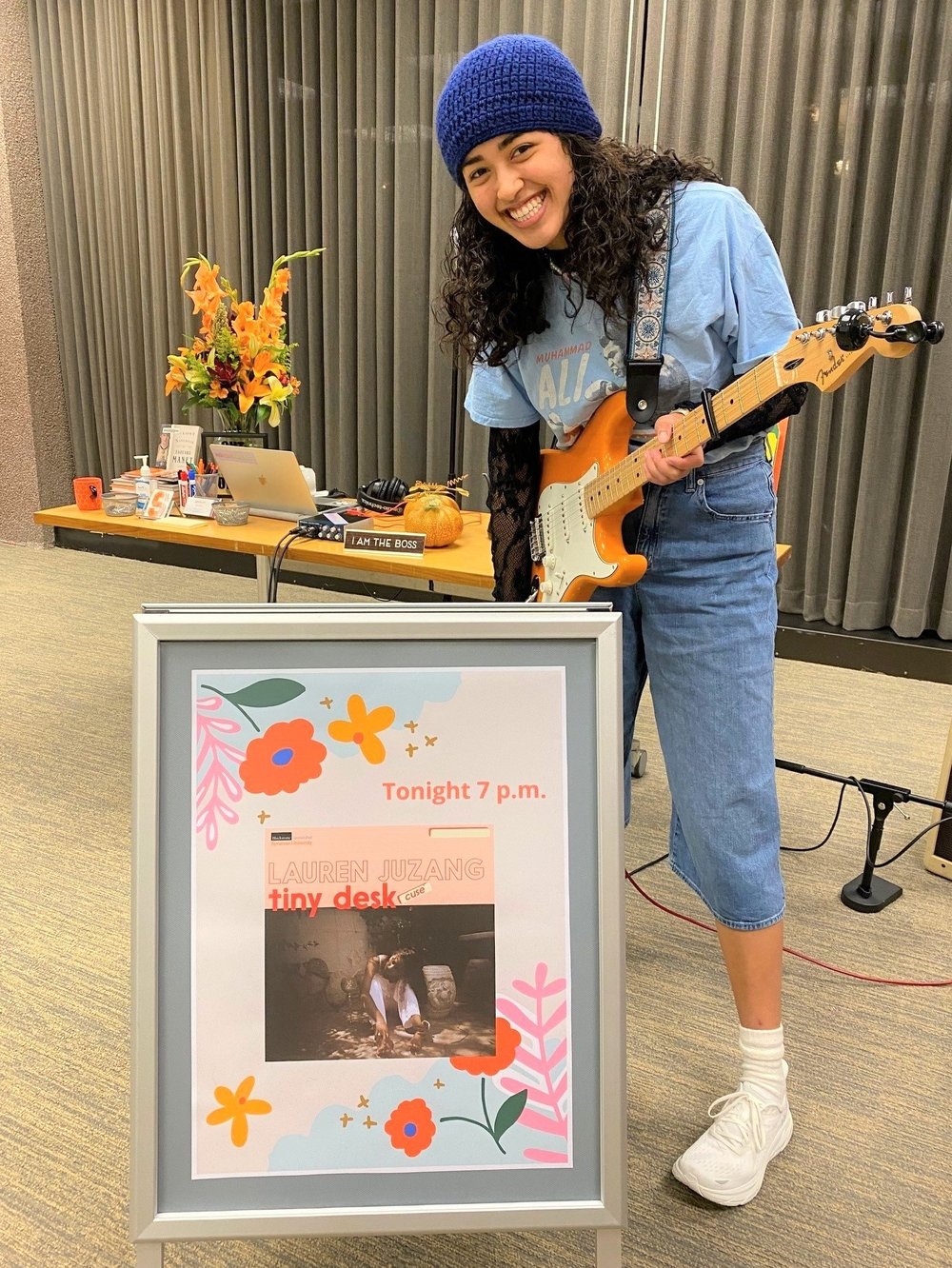 Lauren Juzang holding a guitar, standing in front the tiny desk sign