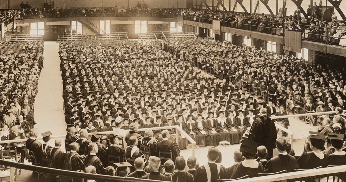 Sepia tone photograph of Chancellor James Roscoe Day speaking at Commencement ceremony in Archbold Gymnasium, 1916, with large crowd of graduates looking on. From the Syracuse University Photograph Collection, University Archives
