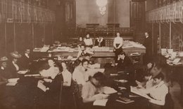 Interior of the von Ranke Library, circa 1900, in sepia tone with people sitting at tables and several people standing behind a large counter