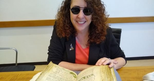 person wearing sunglasses and sitting in front of open medieval book