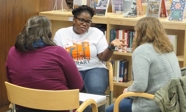 Three people sitting in chairs and talking in front of a book shelf