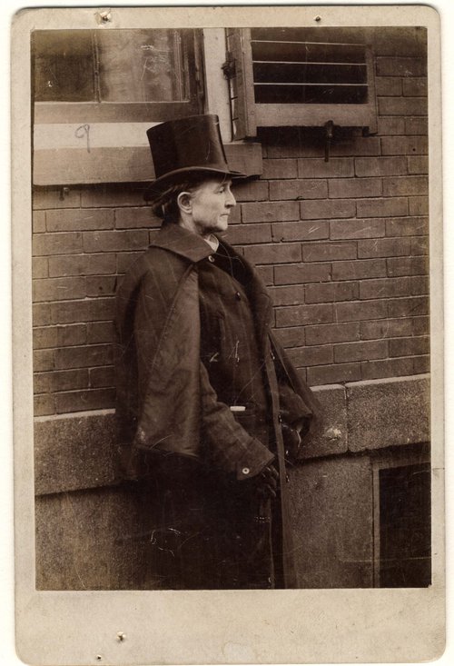 Mary Edwards Walker standing next to building, wearing top hat and men’s overcoat, undated. Mary Edwards Walker Papers.