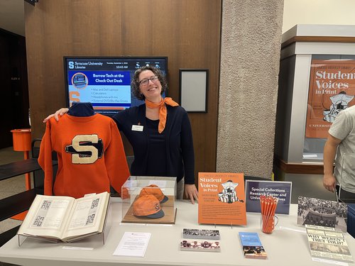 Meg Mason posing next to orange block s sweater and behind table with materials from archives