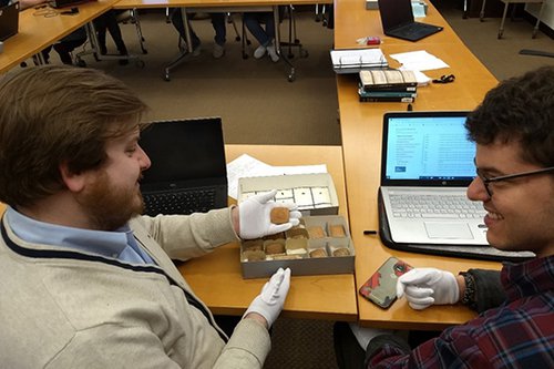 Students wearing white gloves look at cuneiform tablet