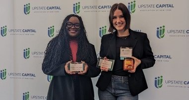 2 females holding awards standing in front of Upstate Capital banner