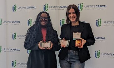 2 females holding awards standing in front of Upstate Capital banner
