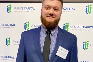 headshot with Upstate Capital Association of New York banner in background