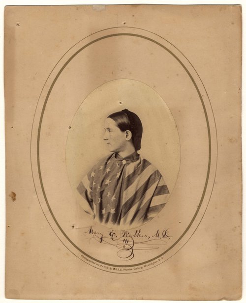 Oval portrait photograph of younger Walker, left profile, wearing American flag draped over her shoulders, handwritten below is “Mary E. Walker, M.D.” photographed by Paige & Mills, Washington, D.C. Mary Edwards Walker Papers.