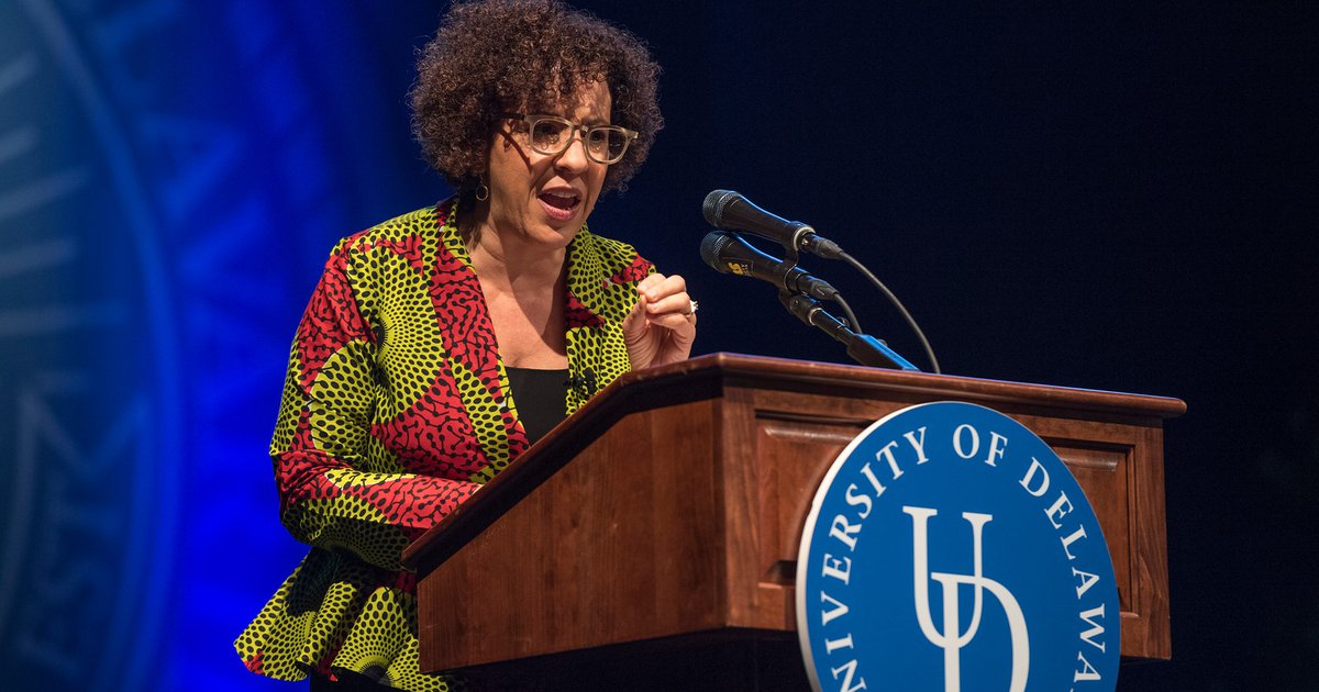 P. Gabrielle Foreman speaking at a wooden podium with blue University of Delaware seal and backdrop