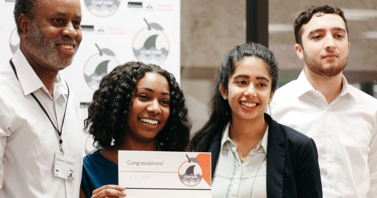 Three student entrepreneurs posing with a mentor and a winning check at a Blackstone LaunchPad business competition