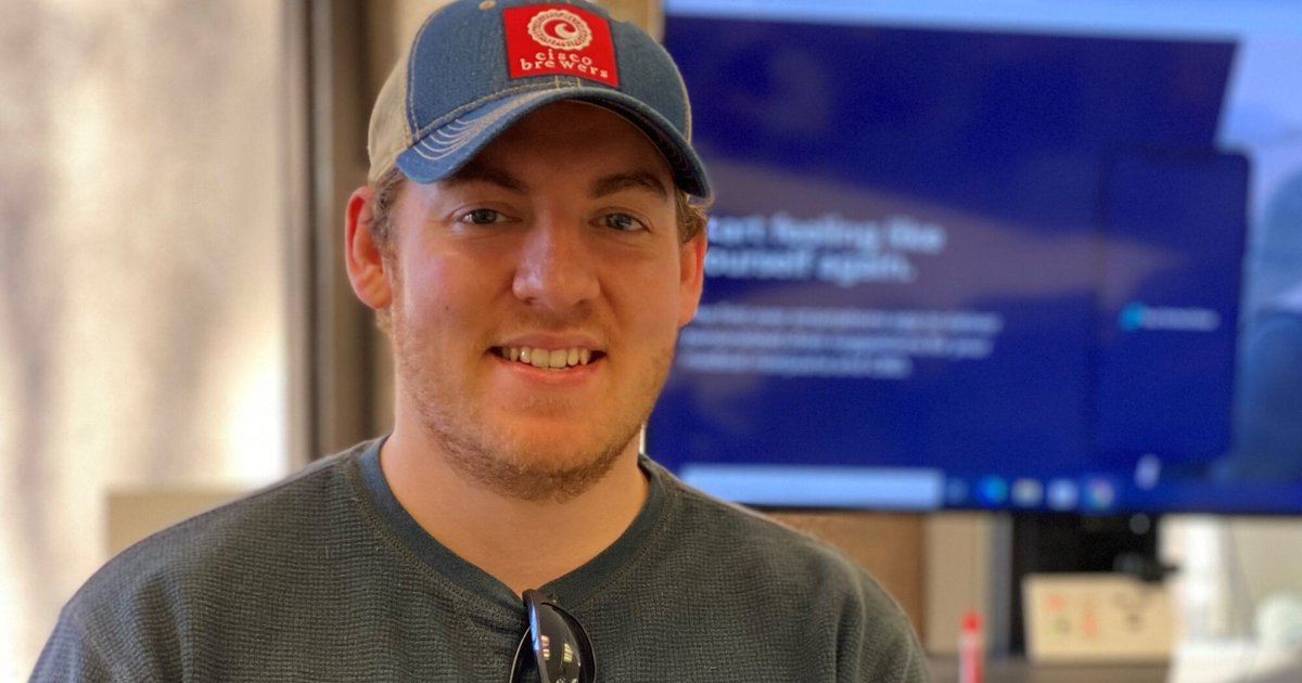 Patrick Prioletti in blue long sleeve shirt and baseball hat smiles for a photo