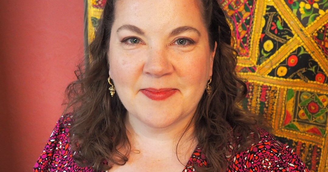 headshot with colorful tapestry behind person