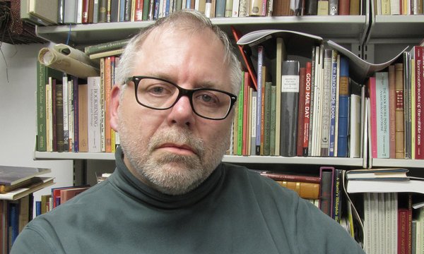 Peter Verheyen sitting in front of a book shelf wearing glasses and a gray turtleneck