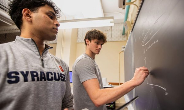 two students writing on chalkboard