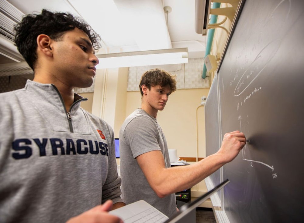 two students writing on chalkboard