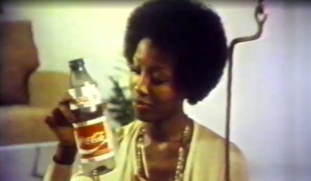 Archival screenshot from a Easy Goer Lightweight Plastic Bottles advertisement circa 1975, with a Black woman holding a plastic Coca Cola bottle