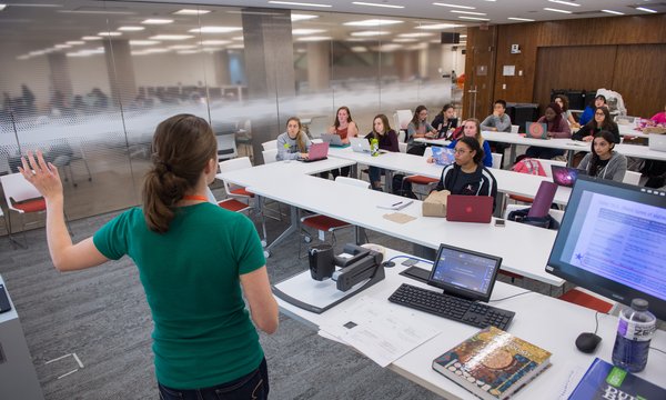 Instructor leading a classroom of students sitting at long white tables