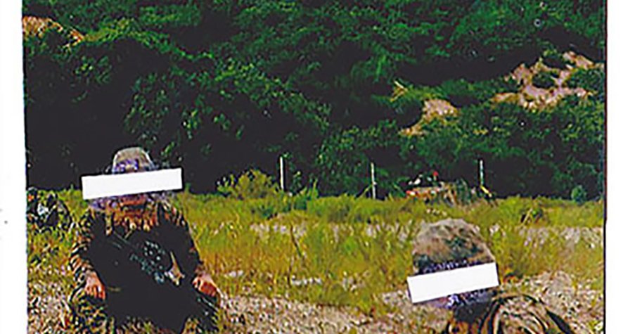 photo of two people on grass with colorful mountain in background