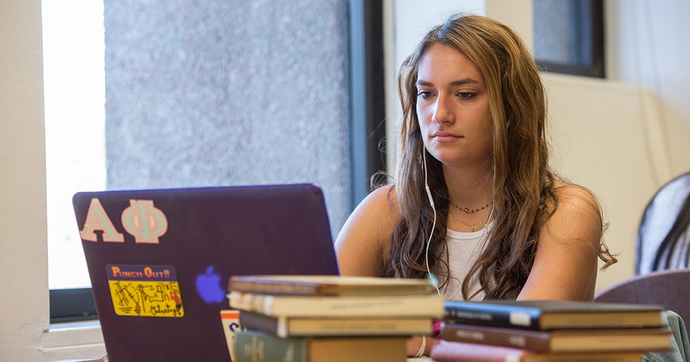 student working on a laptop with stacks of books