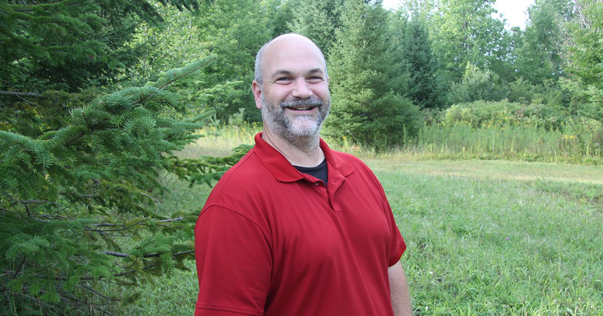 Russell Silverstein in a red shirt standing in front of grass and trees