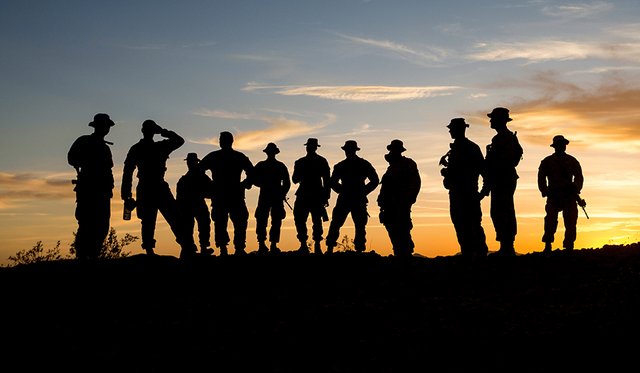 Sunset background with silhouetted group of 11 soldiers on a grassy hill