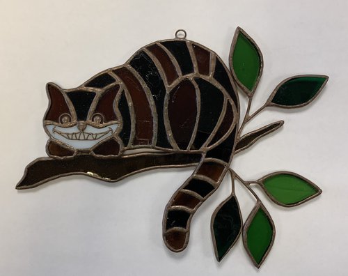 Stained glass memorabilia of Cheshire Cat perched on a tree branch. Kay Rossman Collection of Alice in Wonderland Memorabilia.