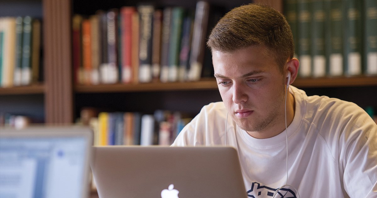 student looking at computer, books behind him