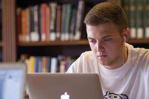 Student wearing earbuds and working on an Apple laptop