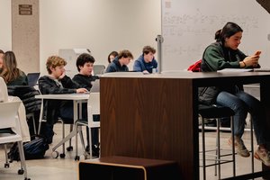 Students working at tables on the lower level of Bird Library, with one student in the front browsing her cell phone