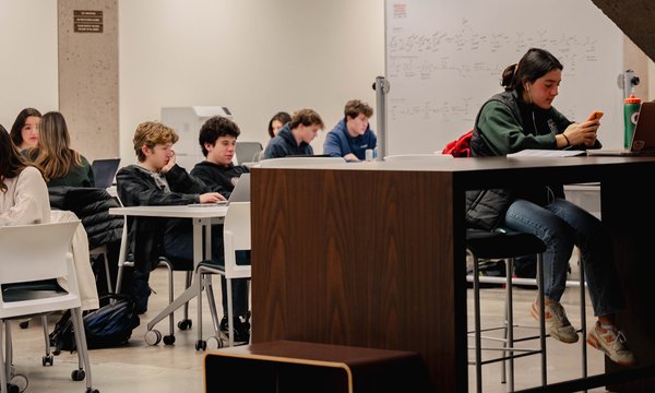 Students working at tables on the lower level of Bird Library, with one student in the front browsing her cell phone