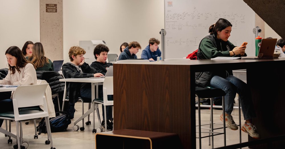 Students working at tables on the lower level of Bird Library, with one student in the front browsing her cell phone