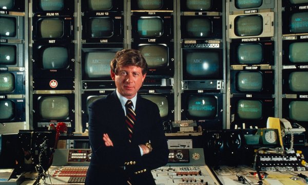 Ted Koppel standing in front of dozens small television screens