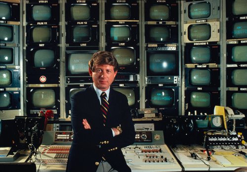 Ted Koppel, newscaster, sitting in front of wall of mini television screens