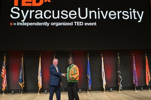 two people shaking hands on stage with sign behind them that reads TEDx Syracuse University