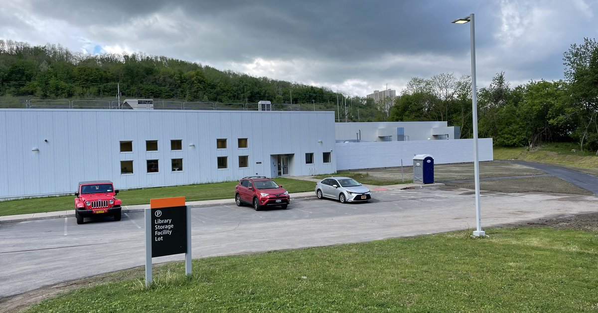 one story white building with cars and grass in front, gray clouds overhead